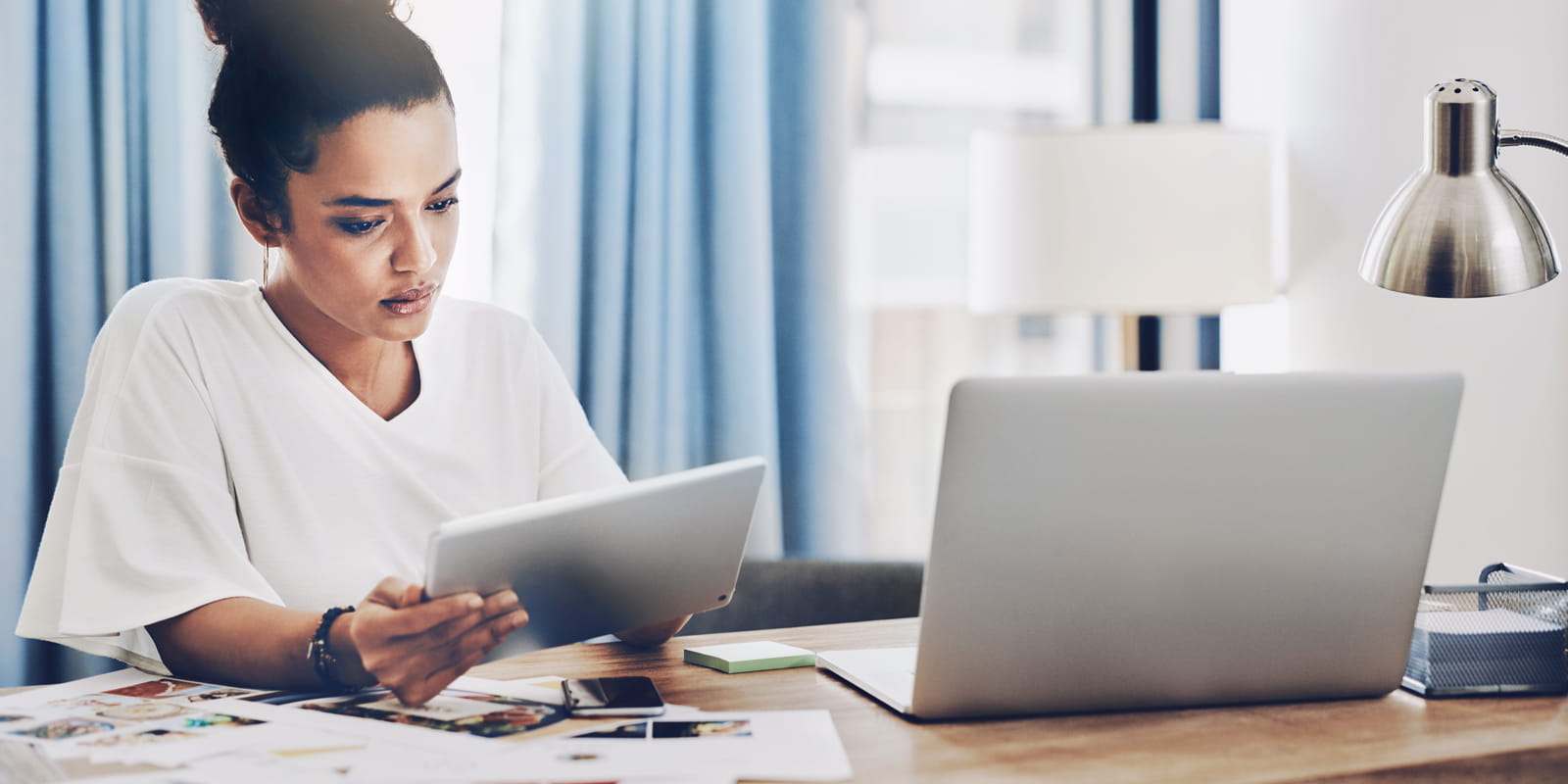 woman looking at tablet with laptop on desk