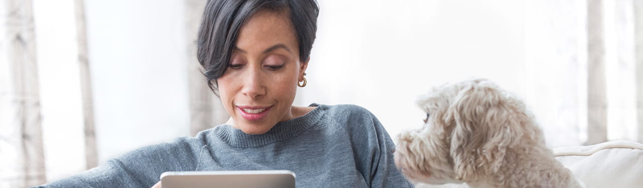Woman on the couch with her dog, looking at a tablet